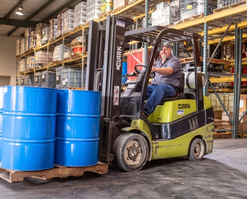 Hutchens team member driving a forklift loaded with a palette of 50 gallon drums containing lubricants