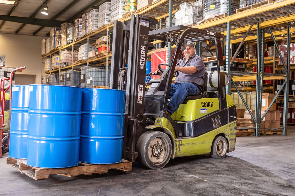 Hutchens team member driving a forklift loaded with a palette of 50 gallon drums containing lubricants